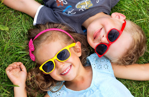 Boy and girl laying on down grass wearing their sunglasses