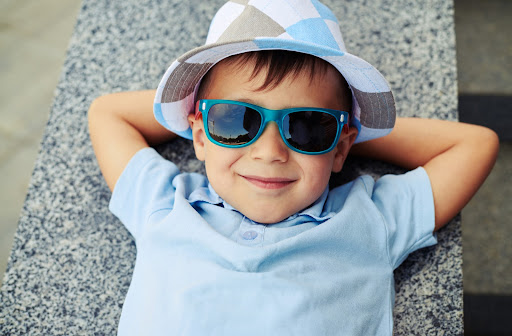 Young boy laying down wearing sunglasses and a hat.