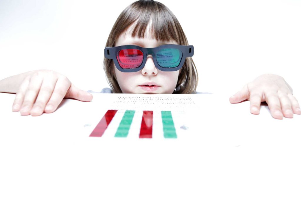 A child with red green reading bar and glasses. An activity requires both eyes to work together to react to the target or read text with the red/green overlay, Mainly used for stress-related myopia to help with the muscles in the eyes.