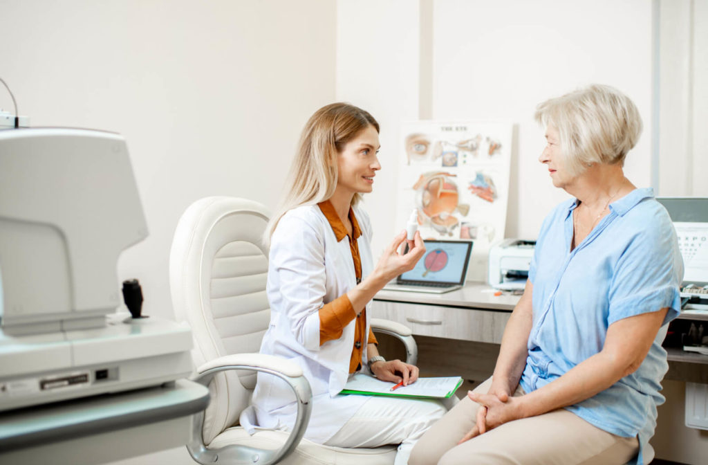 An eye doctor is sitting face to face on her senior patient and asking questions during an eye exam.