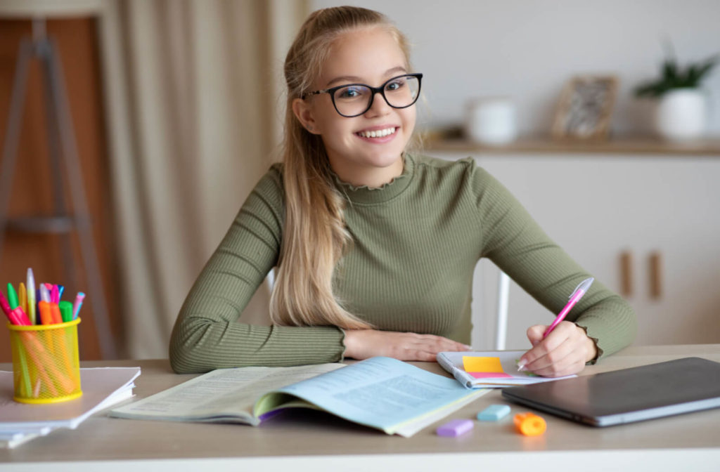 A young girl student is wearing eyeglasses while doing her homework .