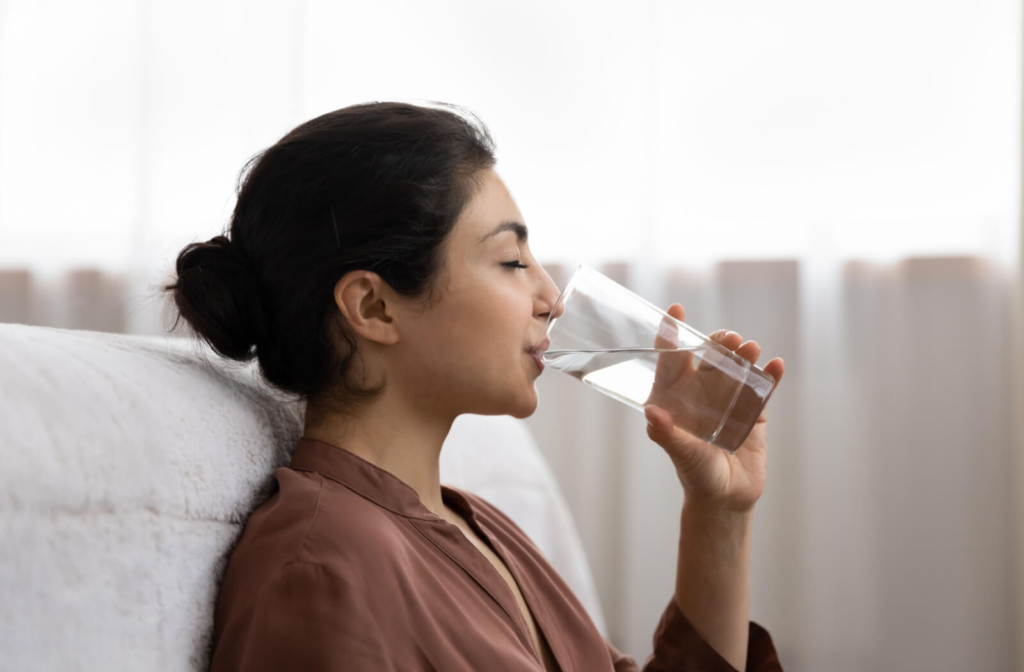 Young woman drinking a glass of water in her living room.