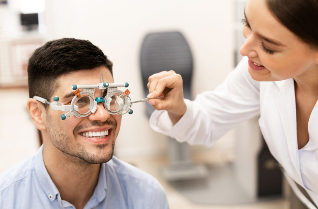 A patient smiling and wearing a trial frame device while his female optometrist happily makes adjustments