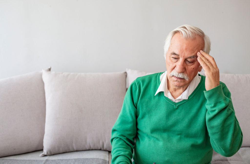 A senior person in a green sweater suffering from a headache while sitting on a couch.