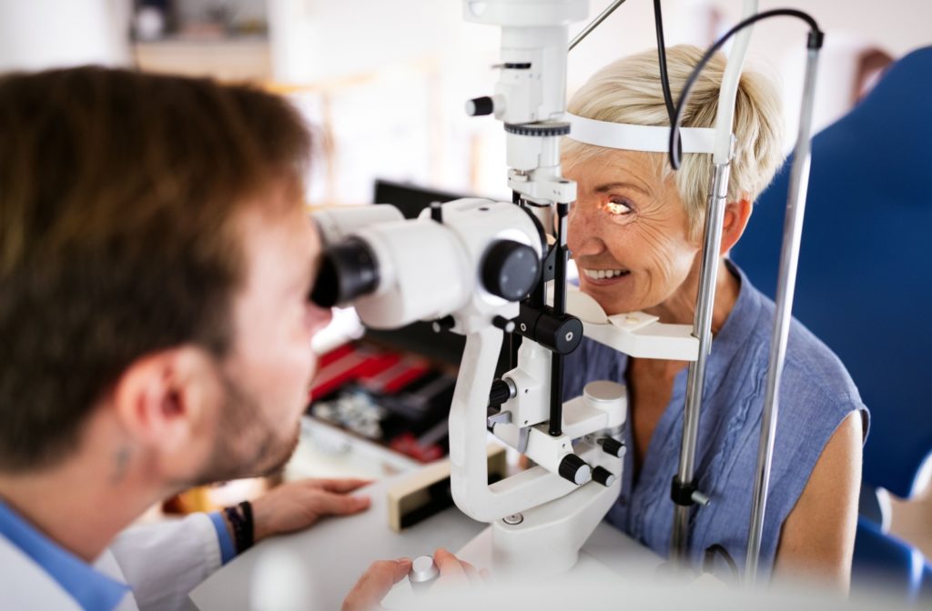 An older woman sits at a slit lamp and has her eye health examined by an optometrist.