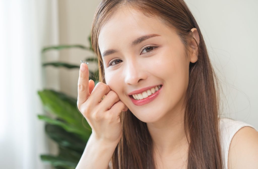 A smiling young woman holding a specialty contact lens on the tip of her right index finger.