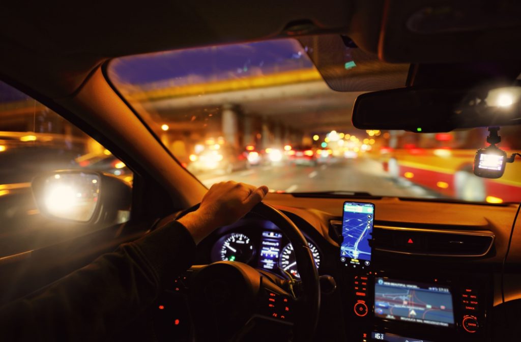 The interior of a car with the dashboard lit up, glare on the rearview mirrors, and glare on the exterior traffic