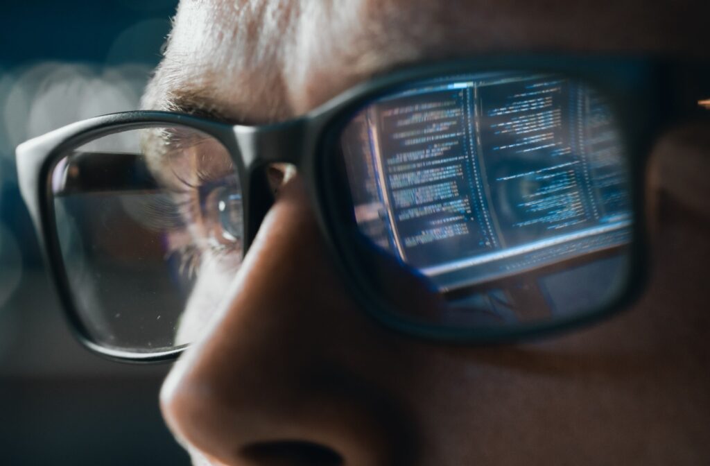 Close-up of a person wearing glasses with a computer screen reflected in the lenses.