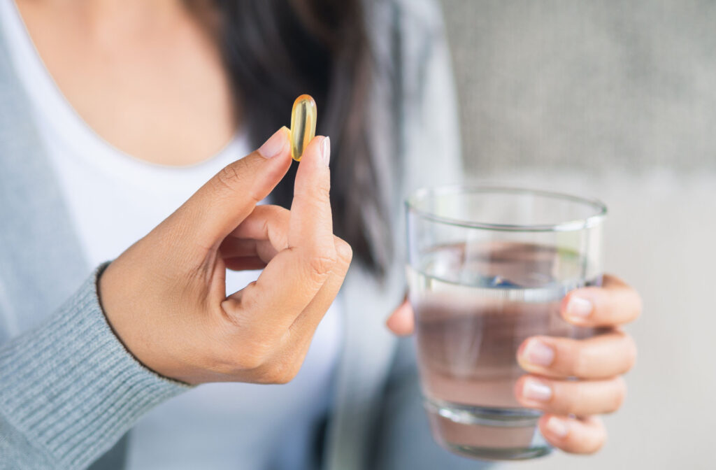 A hand holding a cup of water and a omega-3 vitamin to help with the symptoms of dry eye.