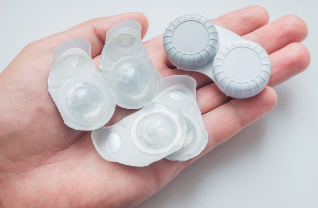 A hand holding daily contact lenses in blister packs and monthly contact lenses in a contact lens case.