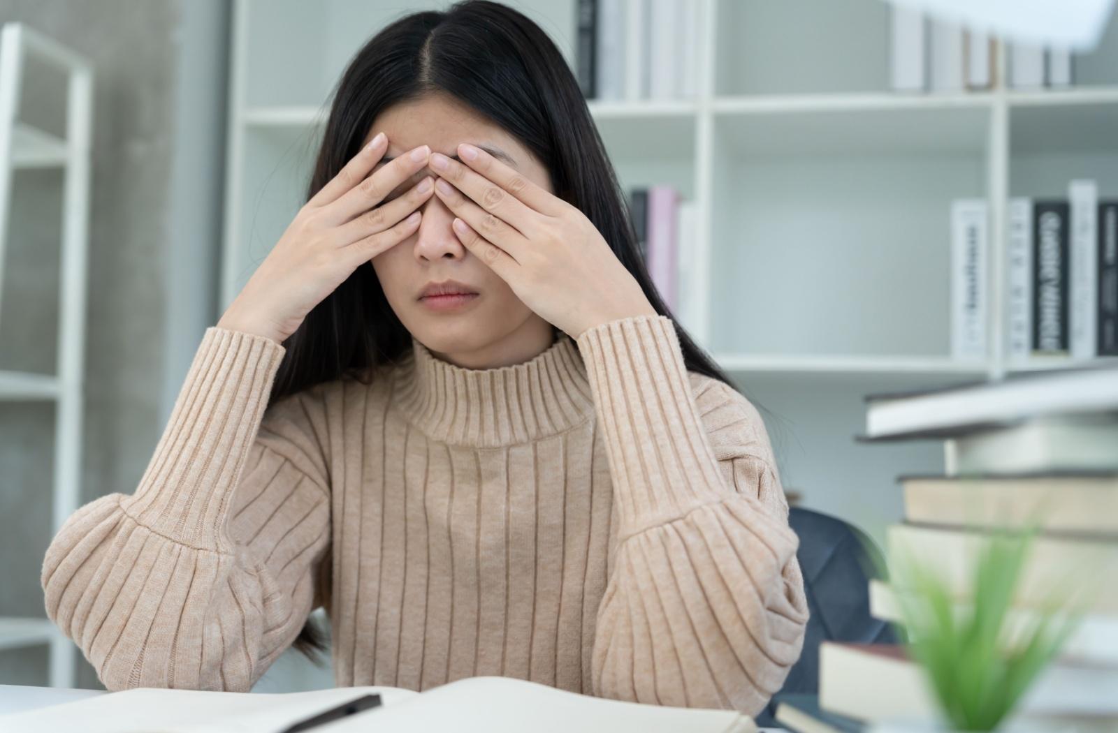 A person sitting at a desk, holding their eyes because their experiencing symptoms of dry eye.